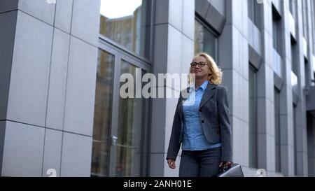Lächelnd Senior Business Lady mit Aktenkoffer geht zur Arbeit, Politikerin Stockfoto