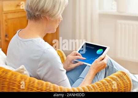 Ältere Frau in ihrem Wohnzimmer ihrer Investment Portfolio die Überprüfung auf einen Tablet-PC. Stockfoto