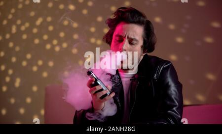 Entspannt hipster Mann vaping e-Zigarette an Rave Party im Night Club, schlechte Gewohnheiten Stockfoto