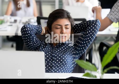 Ruhige junge indische Büroangestellter in Stuhl, die Hände über dem Kopf, die Pause vom anstrengenden Arbeit zu entspannen, erschöpft weiblicher Angestellter Rest am Arbeitsplatz, Einschlafen Stockfoto