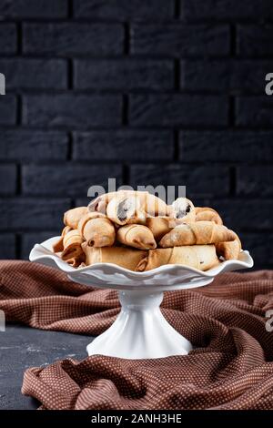 Frisch gebackene Mini-croissants mit Mohn und Rosinen füllen auf einem weißen Kuchen stehen auf einer konkreten Tabelle mit einer Mauer im Hintergrund, Clos Stockfoto