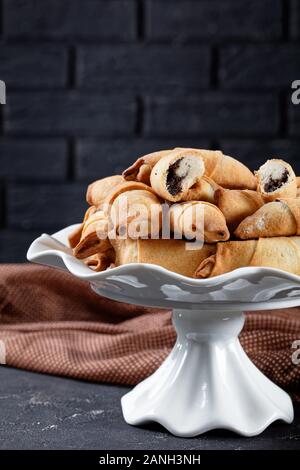 Frisch gebackene Mini-croissants mit Mohn und Rosinen füllen auf einem weißen Kuchen stehen auf einer konkreten Tabelle mit einer Mauer im Hintergrund, Clos Stockfoto