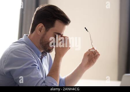 Müde männliche Mitarbeiter nehmen Sie Gläser massieren Nasensteg leiden unter Kopfschmerzen, die erschöpften Menschen Müdigkeit in verschwommene Sicht oder der Sicht Probleme, Stockfoto
