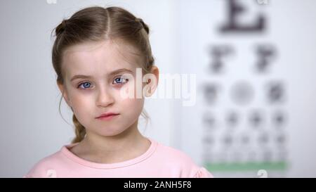 Trauriges kleines Mädchen mit roten Augen auf die Rezeption des Augenarztes, Sehstörungen Stockfoto