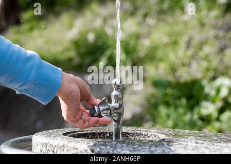 Eine Hand, die einen öffentlichen Trinkbrunnen hält. Wasser, das nach oben spritzt. Stockfoto