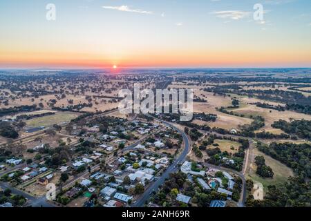 Landstraße schlängelt sich durch Wiesen und kleine Stadt im australischen Hinterland - Luftbild panorama Stockfoto
