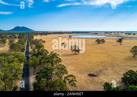 Gerade Landstraße führt zu einem Berg zwischen Feldern und Bäumen in Australien Stockfoto