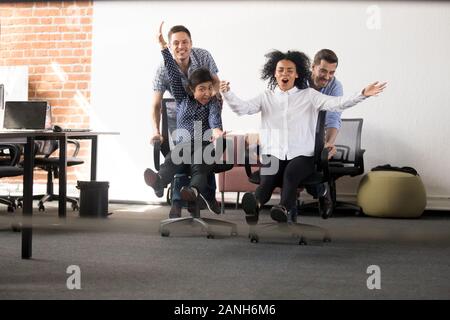 Aufgeregt multirassischen junge Mitarbeiter haben Spaß im Büro, auf Stühlen das Rennen , diverse Arbeiter unterhalten lachend am Arbeitsplatz engagieren Stockfoto