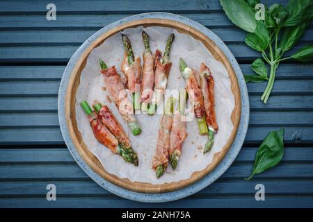 Buffet - Parmaschinken und Mozzerella umhüllter Spargel auf einem Teller auf einer blauen Picknickbank. Flaches Lay Stockfoto