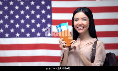 Aufgeregt Frau mit Reisepass und Flugtickets gegen USA-Flagge im Hintergrund Stockfoto