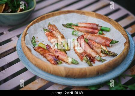 Buffet - Parmaschinken und Mozzerella umhüllter Spargel auf einem Teller auf einer pinkfarbenen Picknickbank. Flaches Lay Stockfoto