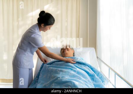 Ältere Frau im Bett und Krankenschwester decken Decke zu ihr. Alte asiatische Frau und schöne asiatische Krankenschwester Frau im Schlafzimmer Service Konzept in der Altenpflege center Stockfoto