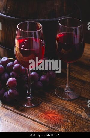 Zwei Gläser Rotwein und Trauben auf einem Holztisch mit Holz Fass im Hintergrund Stockfoto