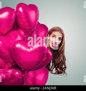 Pretty Woman späht aus rosa Herz Ballons und Lachen Stockfoto