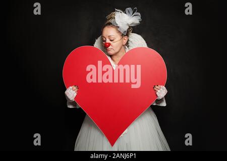 Schauspielerin Dame in Clown Kostüm mit roten Herzen auf schwarzem Hintergrund Stockfoto