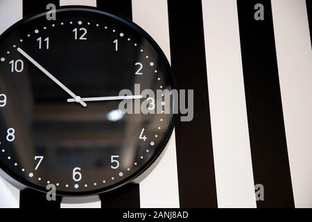 Große schwarze Uhr auf die gestreifte Wand des Raumes Stockfoto