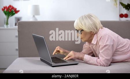 Alte Frau in Brillen aufmerksam, indem Sie auf Laptop, App für ältere Menschen Stockfoto