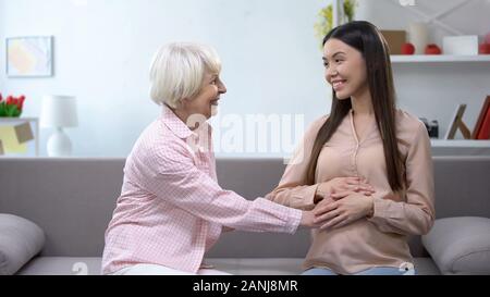 Lächelnde ältere Frau mit enkeltochter Bauch halten, Schwangerschaft, familiäre Betreuung Stockfoto
