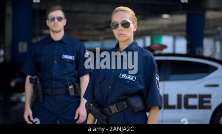 Ernsthafte Frau und Mann Polizeibeamte in Sonnenbrille ständigen Außeneinsatz, Sicherheit Stockfoto