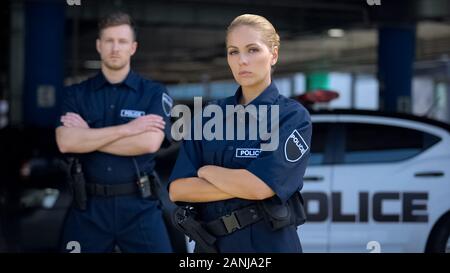 Qualifizierte Polizeioffiziere auf Hintergrund der Streifenwagen posiert, Strafrecht Stockfoto