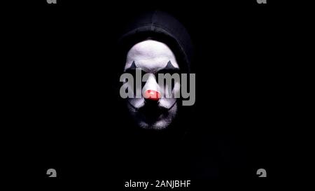 Spooky Clown in Hoodie bei Camera suchen, schwarzer Hintergrund, kriminelle verschleiern Stockfoto