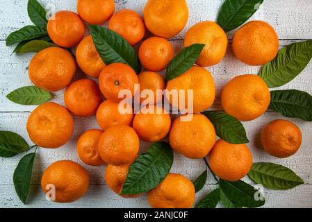 Gruppe der ganzen hellen orange Mandarinen Mandarinen mit frischen grünen Blätter auf alte weiße Holztisch Oberfläche gerissen. Früchte und Blätter haben natürliche im Stockfoto