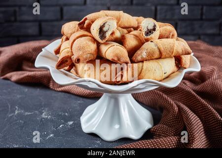 Frisch gebackene Mini-croissants mit Mohn und Rosinen füllen auf einem weißen Kuchen stehen auf einer konkreten Tabelle mit einer Mauer im Hintergrund, Clos Stockfoto