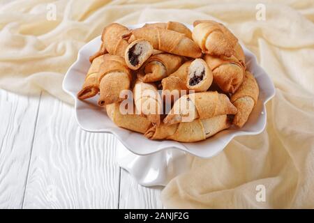 Frisch gebackene Mini-croissants mit Mohn und Rosinen füllen auf einem weißen Kuchen stehen auf einer konkreten Tabelle mit einer Mauer im Hintergrund, Clos Stockfoto