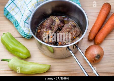 Traditionell hergestellt Rindersteaks in Sauce mit Karotten und Zwiebeln als closeup in einem gusseisernen Topf geben auf einen hölzernen Tisch angeboten Stockfoto