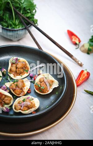 Asiatische Kichererbsenform mit Chili und Koriander. Serviert auf einem schwarzen Gericht mit weißem Holzhintergrund, mit Essstäbchen Stockfoto