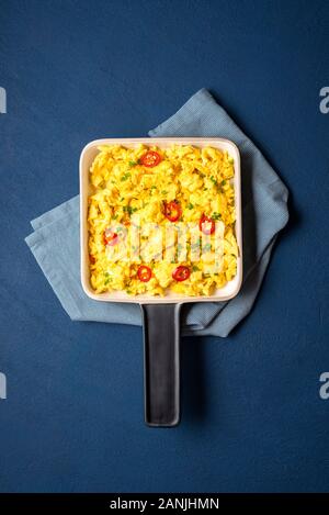 Eier in einem keramischen Pfanne mit Chili peppers am Phantom blue Tabelle Rührei. Über anzeigen und eine Nahaufnahme von Rührei. Leckeres Frühstück. Protein Food. Stockfoto