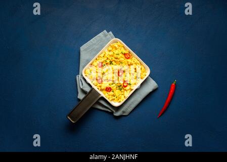 Warme Rühreier mit Chili peppers auf einem Küchenpapier, auf Classic blau Tischplatte. Oben Blick auf Rührei in der Pfanne. Minimale Bild von Frühstück. Stockfoto