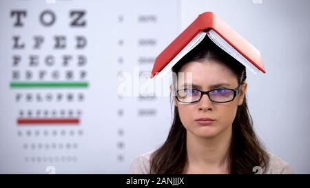 Dame mit Buch auf den Kopf in die Kamera schauen, überarbeitete Student die Vorbereitung für die Prüfung Stockfoto