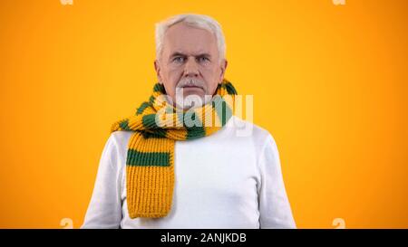 Kranke ältere Mann in Schal gegen orange Hintergrund, Bronchitis Symptom Stockfoto