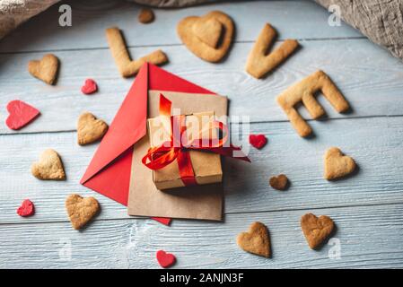 Nachricht von einem süßen Cookie in Form des Wortes Liebe und ein Geschenk mit roter Schleife ein blauer Hintergrund Holz gebunden. Romantischer Valentinstag Geschenk Stockfoto