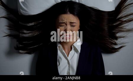 Asiatische Frau in Anzug im Bett weinen, leiden Paranoia von Überlastung Stockfoto