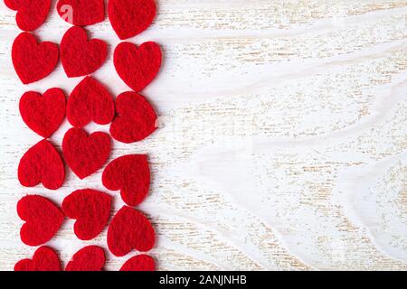 Viele rote Filz Herzen zum Valentinstag auf der linken Seite des weißen Holz texturierte Oberfläche. Gruß Valentine Karte mit kopieren. Romantik und Liebe Konzept. Stockfoto