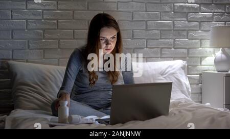 Lady lesen Pillen Anweisungen auf Laptop, den Glauben im Internet Werbung Stockfoto