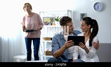 Neugierig Schwiegermutter Suche junges paar Scrollen auf Tablet-PC zu Hause Stockfoto