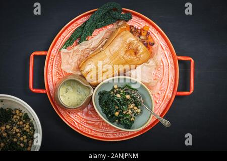 Gebratener Butternusskürbis mit Kale- und Kichererbsensalat. Gesunde vegane Speisen werden auf einem orangefarbenen Tablett mit schwarzem Hintergrund serviert. Draufsicht / flache Lage Stockfoto