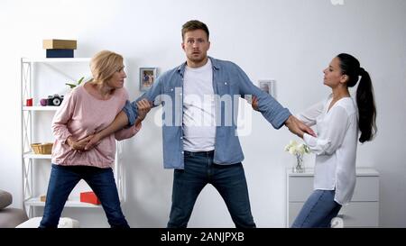 In Konflikt, Mutter und Ehefrau ziehen junge Mann in verschiedene Richtungen. Stockfoto