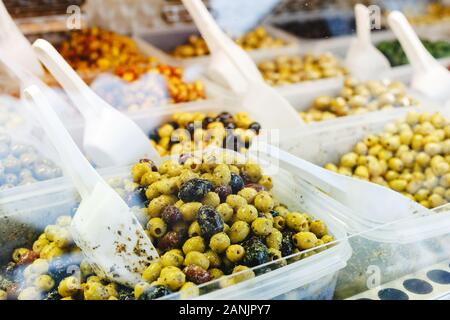 Verschiedene Arten von Oliven im Markt. Mix grün, schwarze Oliven mit Knoblauch, Pesto, Kräuter auf einen Zähler mit einem Messlöffel zum Verkauf. Foto traditio Stockfoto