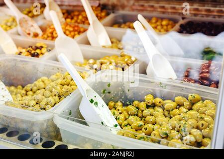 Verschiedene Arten von Oliven im Markt. Mix grün, schwarze Oliven mit Knoblauch, Pesto, Kräuter auf einen Zähler mit einem Messlöffel zum Verkauf. Foto traditio Stockfoto