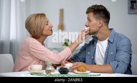 Sorgfältige Mutter abwischen erwachsene Söhne Mund während in Kaffee zu Hause, überbehütung Stockfoto