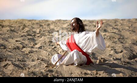 Mönch im Lotussitz heben die Hände zum Himmel, zu Gott zu beten, in der Wüste, Meditation Stockfoto