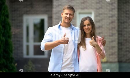 Lächelndes Paar zeigen Daumen hoch stehend gegen Haus, Immobilien Kauf Stockfoto