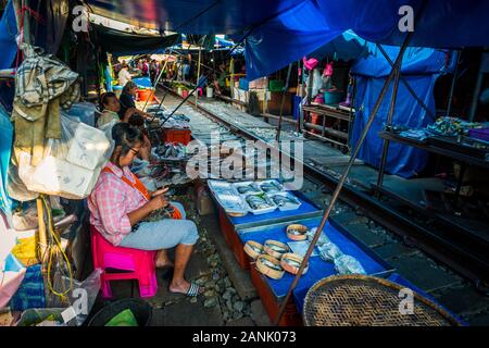 Mae Klong/Thailand-08December2019: Mae Klong Bahnhof mit Gleisen und Zügen, die durch den täglichen Markt führen, mit Anbietern, die alles verkaufen. Stockfoto