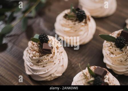 Cremefarbene Pavlova Meringue mit Schokolade liegt auf einer hölzernen alte Tabelle. Schokolade überzogen Baiser Kuchen Rezept auf braunem Grund. Stockfoto