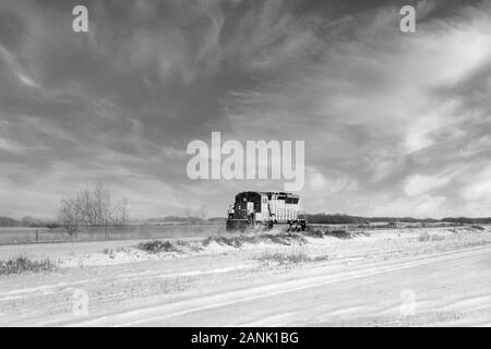 Eine rote Lokomotive auf einer Bahnstrecke in einem bewaldeten Schwarz und Weiß wiese Winter Landschaft Stockfoto