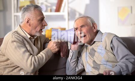 Ältere Menschen schreien Megaphon zu gehörlosen Freund, im Alter Gesundheit, Taubheit Behandlung Stockfoto